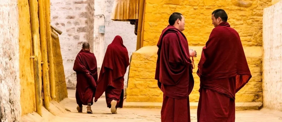 Buddhist monks in maroon robes walk along a sunlit alley with yellow walls.Sera Monastery,Lhasa,Tibet,Chinatravel