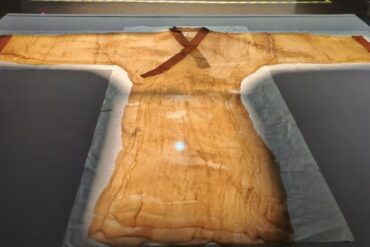 Ancient tan tunic on display in a museum case, with a brown cross-style sash across the chest and long flowing sleeves.Hunan Provincial Museum,Changsha,Hunan ,Chinatravel