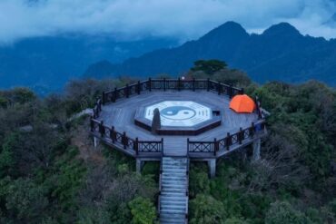 Circular wooden lookout platform on a hill with a large Yin-Yang symbol at center, orange tent to the right, surrounded by mountains and misty blue sky.Sanqing Mountain Scenic Area,Shangrao,Jiangxi,Chinatravel