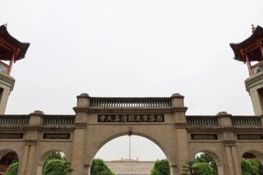 Stone arch gateway in a temple complex, with a central arch flanked by two towers featuring red, pagoda-style roofs and gold Chinese characters on plaques beneath.Dongguan Mosque,Xining,Qinghai