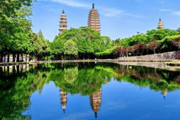 Three-tiered pagodas rise above a green park, reflected in a calm lake.Dali Three Pagodas,Dali,Yunnan,Chinatravel