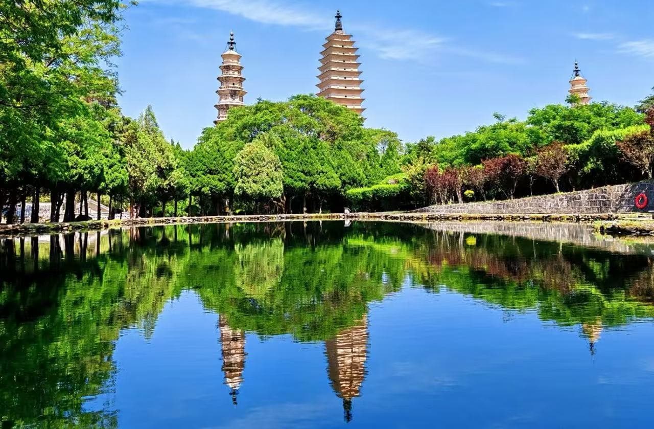 Three-tiered pagodas rise above a green park, reflected in a calm lake.Dali Three Pagodas,Dali,Yunnan,Chinatravel