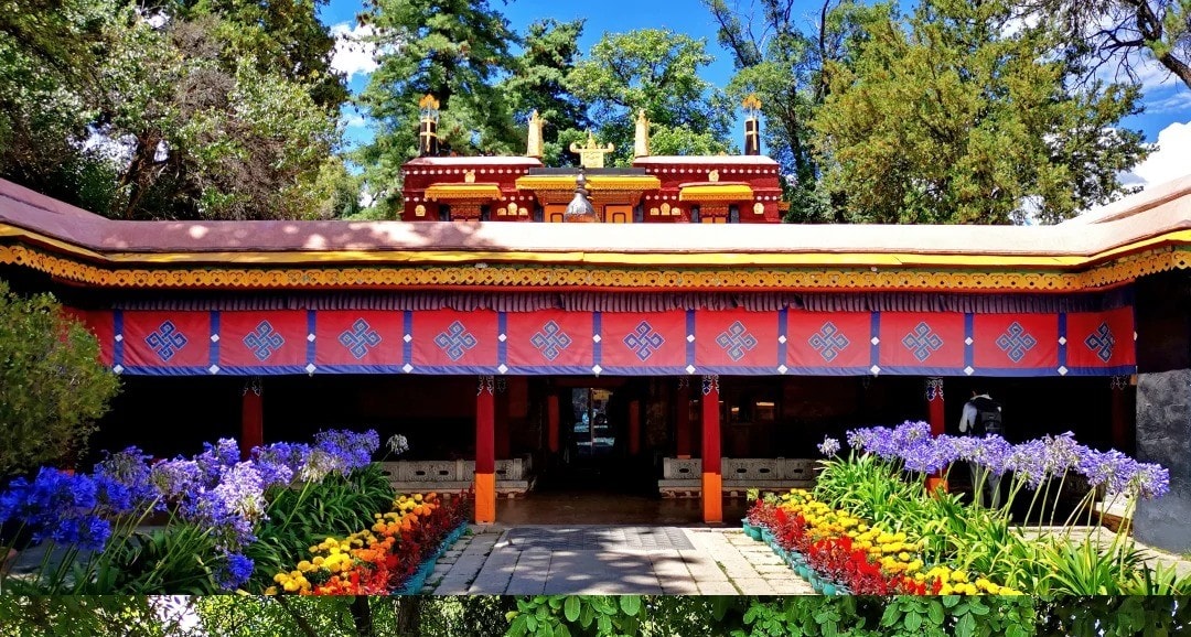 Colorful temple entrance with red canopy, decorative patterns, and blooming purple, yellow, and red flowers lining a stone path,Norbulingka Park,Lhasa,Tibet,Chinatravel