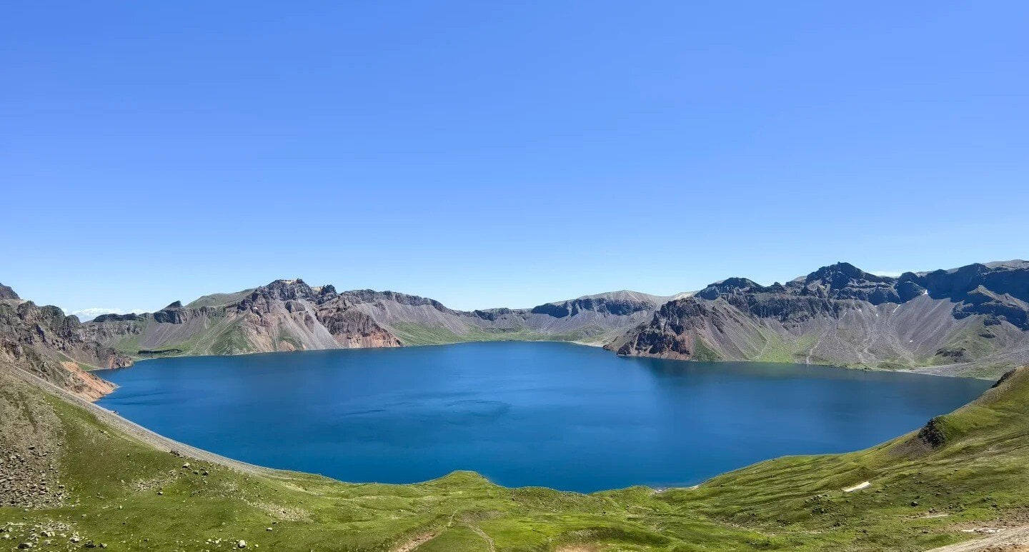 Baishan West Slope Scenic Area,Baishan,Jilin,Chinatravel Bright blue alpine lake nestled in a circular crater, with green slopes and rugged mountain peaks under a clear sky.