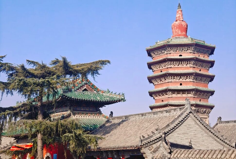 Wenfeng Pagoda,Anyang,Henan,Chinaexplorertour Seven-story red brick pagoda with green-tiled eaves stands beside traditional Chinese temple roofs under a clear blue sky.