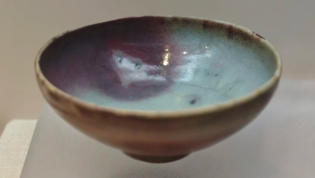 Henan Kaifeng Museum,Kaifeng,Henan,Chinatravel Handmade ceramic bowl with a glossy blue-green to purple glaze inside, viewed from the side on a neutral surface.