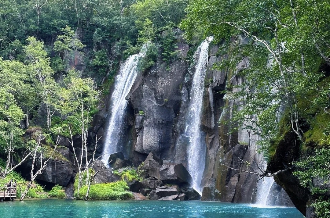 Baishan North Slope Scenic Area,Baishan,Jilin,Chinatravel Waterfall cascade over rocky cliff into a turquoise lake surrounded by green trees.