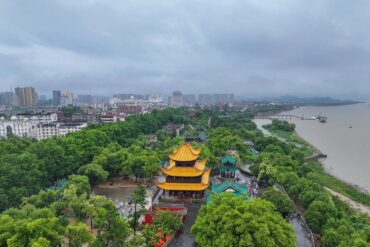 Yueyang Tower,Yueyang,Hunan,Chinaexplorertour Aerial view of a city with a bright yellow multi-tiered pagoda in a green park beside a wide river.