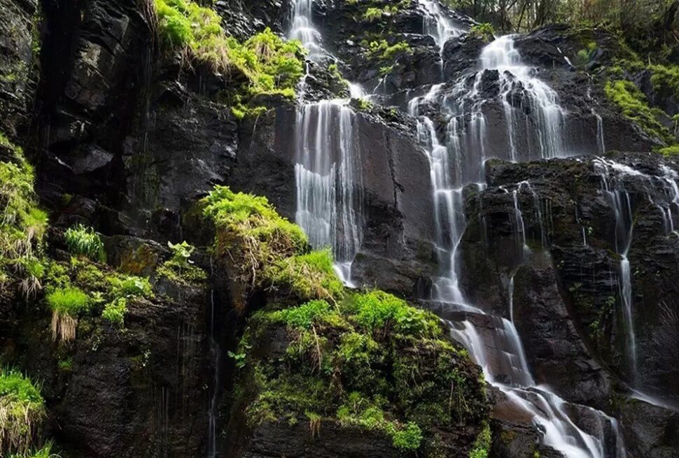 Lushuihe National Forest Park,Baishan,Jilin,Chinatravel Cascade of waterfalls flowing over dark rocks with lush green vegetation on a cliffside.