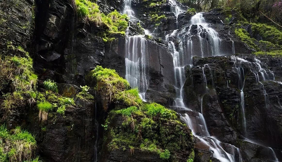 Lushuihe National Forest Park,Baishan,Jilin,Chinatravel Cascade of waterfalls flowing over dark rocks with lush green vegetation on a cliffside.