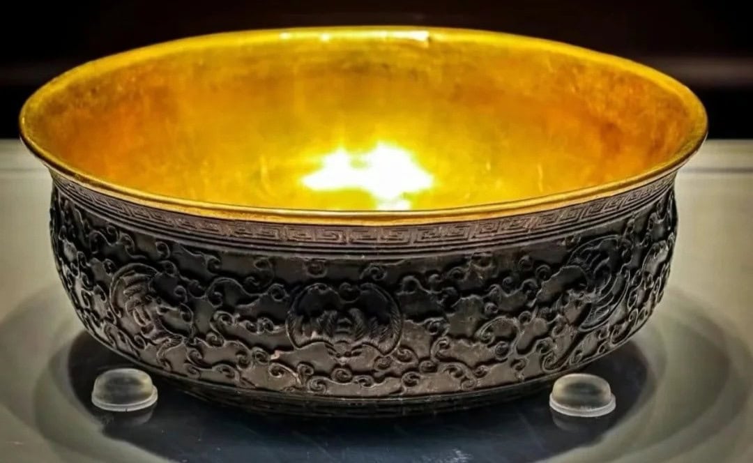 Hainan Museum,Haikou,Hainan,Chinaexplorertour Ornate dark bronze bowl with a gold interior on display, resting on small clear stands.