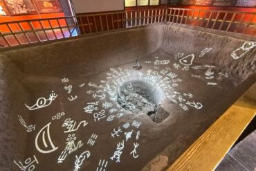 Yin Ruins (Yinxu, UNESCO),Anyang,Chinaexplorertour Indoor museum exhibit: a sunken rectangular pit with a central rock-filled hole, surrounded by white glyphs on the floor and a railing along the edge.