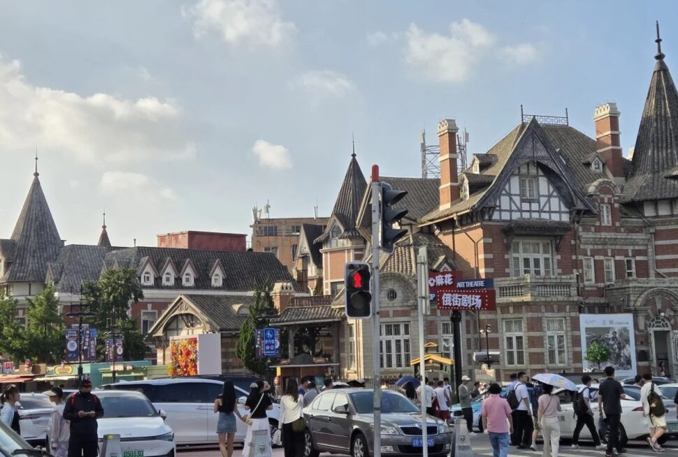 Russian Street (Zhongshan Square),Dalian,Liaoning,Chinatravel Busy urban street lined with ornate brick buildings with steep roofs; pedestrians cross near a traffic light against a blue sky.