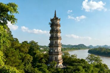 Qingxiu Mountain Ancient Pagoda,Nanning,Guangxi,Chinaexplorertour Tall multi-story pagoda rising through green trees beside a winding river on a clear day, blue sky above.