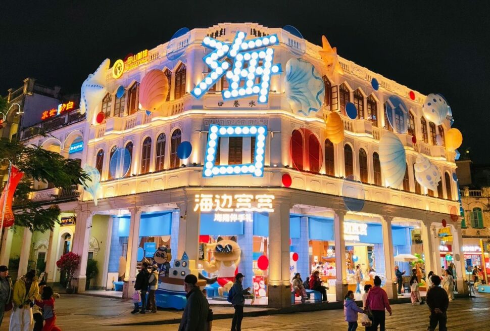Qilou Old Street,Haikou,Hainan,Chinaexplorertour Bright, neon-lit seaside-themed storefront at night with large blue sign and balloons, people walking outside.