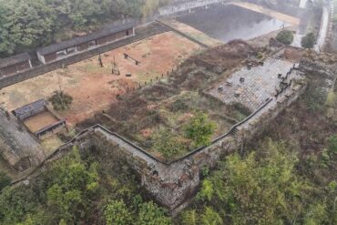 Southern Great Wall Ruins,Fenghuang,Hunan,Chinaexplorertour Aerial view of an old stone fortress with walls, stairways, and a central courtyard amid surrounding trees and hills.