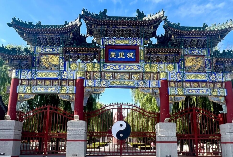 Youli Castle & Scenic Area,Anyang,Henan,Chinaexplorertour Ornate Chinese archway with blue plaque reading '美里城', intricate gold carvings, red pillars, and a yin-yang symbol hanging in front of a gated courtyard.