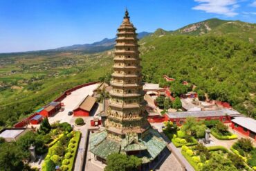 Tall multi-tiered pagoda surrounded by red temple buildings amid green hills and a valley under a blue sky,Guangsheng Temple,Linfen,Shanxi