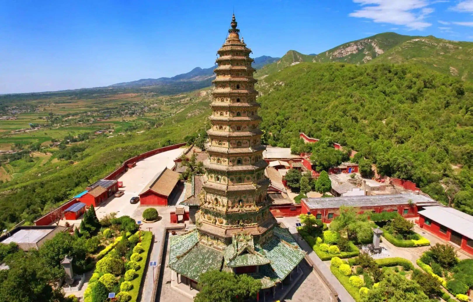 Tall multi-tiered pagoda surrounded by red temple buildings amid green hills and a valley under a blue sky,Guangsheng Temple,Linfen,Shanxi