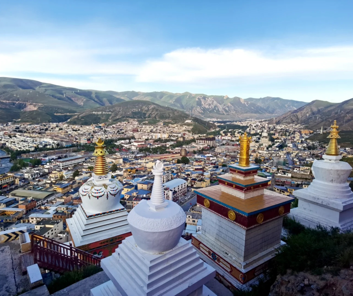 view over a Tibetan town from a hillside with white stupas topped in gold, mountains in the distance under a blue sky,Jyeku Monastery,Yushu, Qinghai