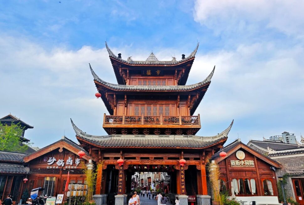 Three-tiered traditional Chinese wooden gate with curved roofs and red lanterns at a pedestrian street entrance.Zhongnanmen Tourism Scenic Area,Tongren,Guizhou