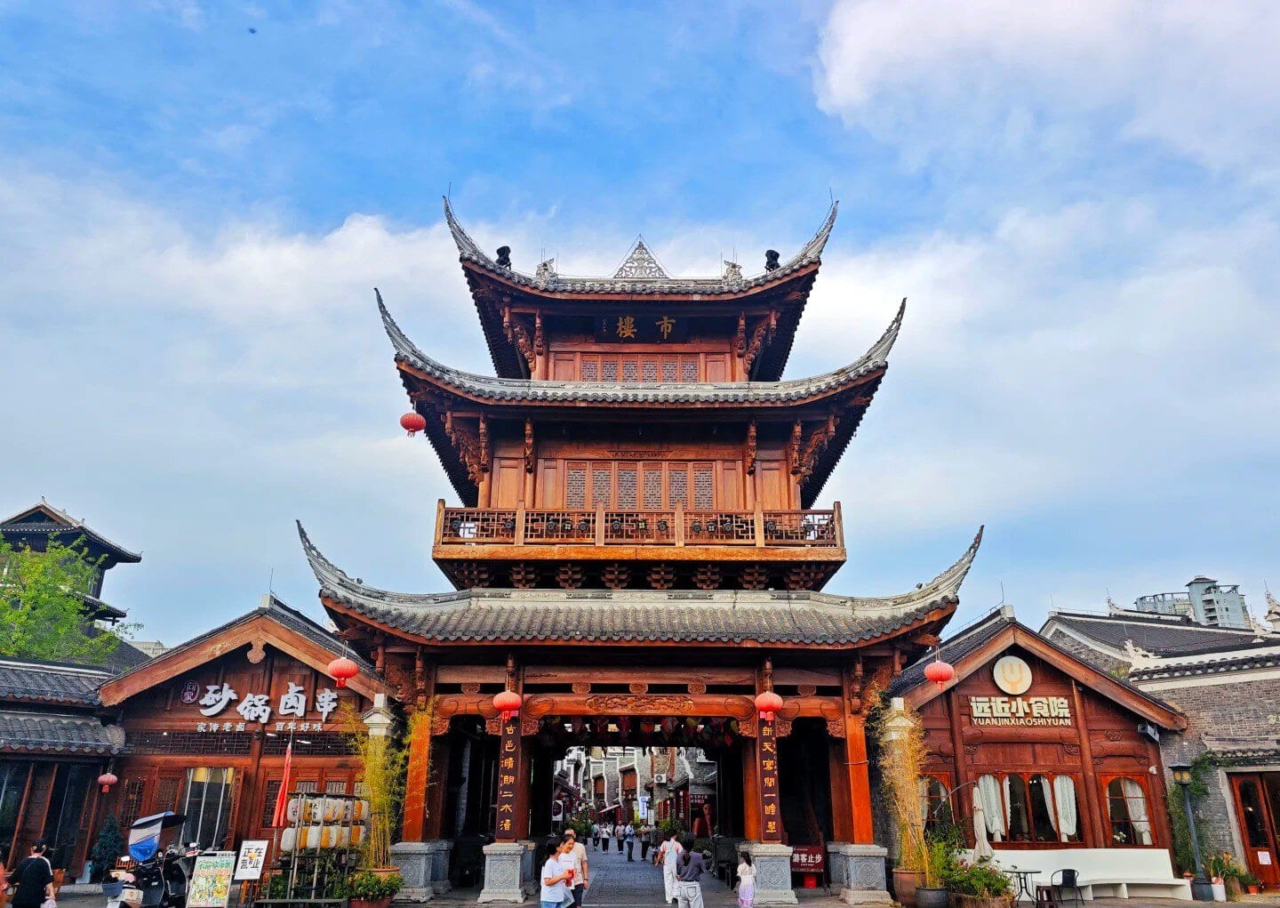 Three-tiered traditional Chinese wooden gate with curved roofs and red lanterns at a pedestrian street entrance.Zhongnanmen Tourism Scenic Area,Tongren,Guizhou