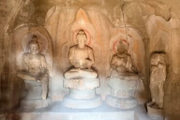 Stone cave shrine with a central seated Buddha flanked by two smaller statues, halos carved in the rock behind them for a devotional display.Tianlongshan Grottoes,Taiyuan, Shanxi