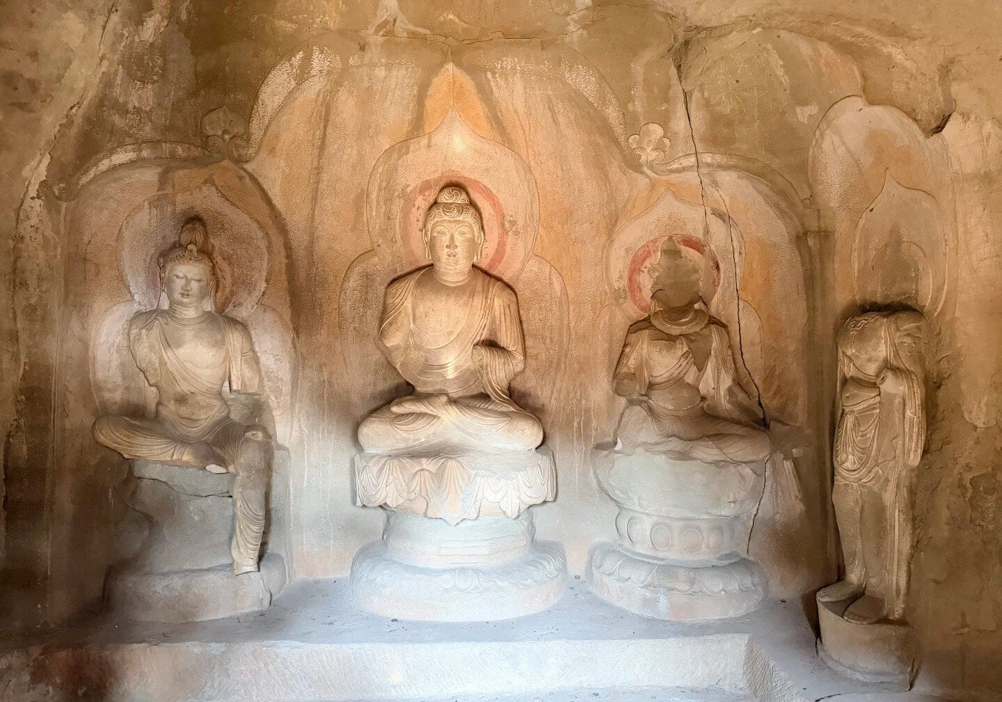 Stone cave shrine with a central seated Buddha flanked by two smaller statues, halos carved in the rock behind them for a devotional display.Tianlongshan Grottoes,Taiyuan, Shanxi