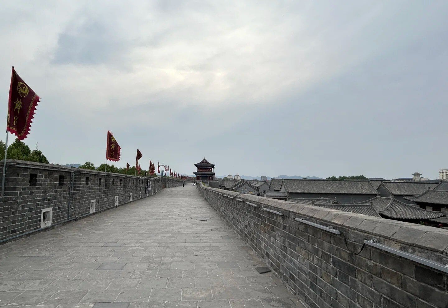 Ancient city wall walkway in China with flags and traditional buildings in the background.