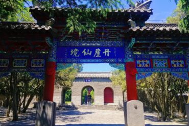 Ornate Chinese temple gate with red columns and blue decorative beams, leading to a brick archway and courtyard,Penglai Pavilion,Yantai,Shandong,Chinatravel