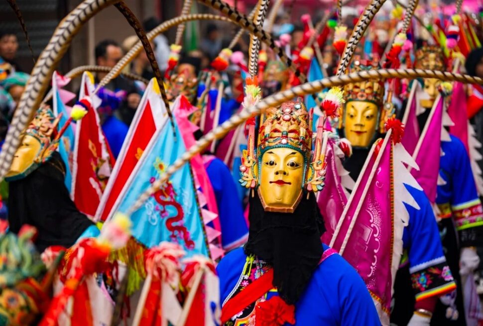 Masked performer in a bright blue outfit with a gold ornate mask leads a colorful festival parade.Anshun Tunpu Cultural Scenic Area ,Anshun,Guizhou