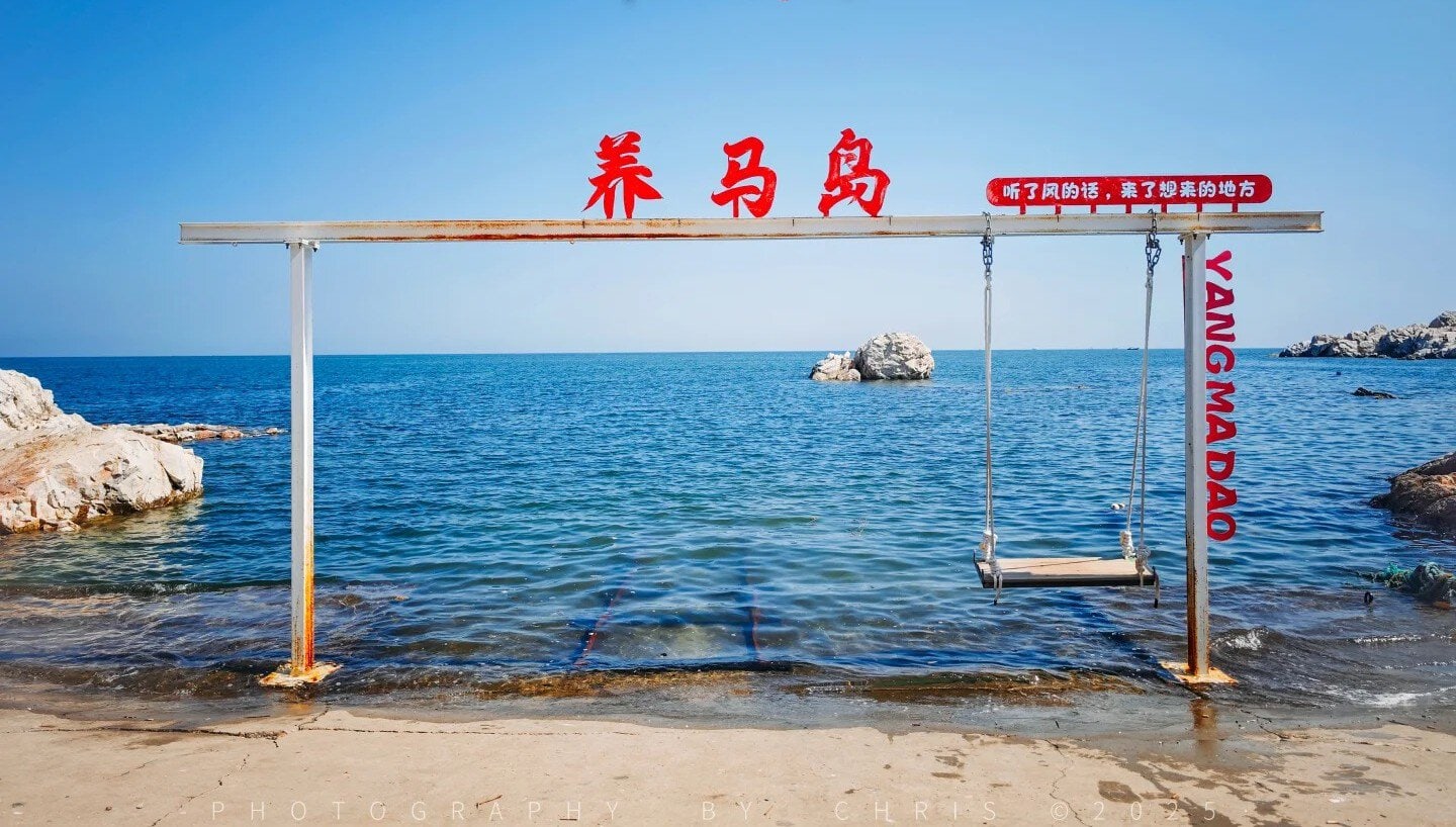 A beach scene with a swing set and red Chinese characters on a wooden beam over the sea.