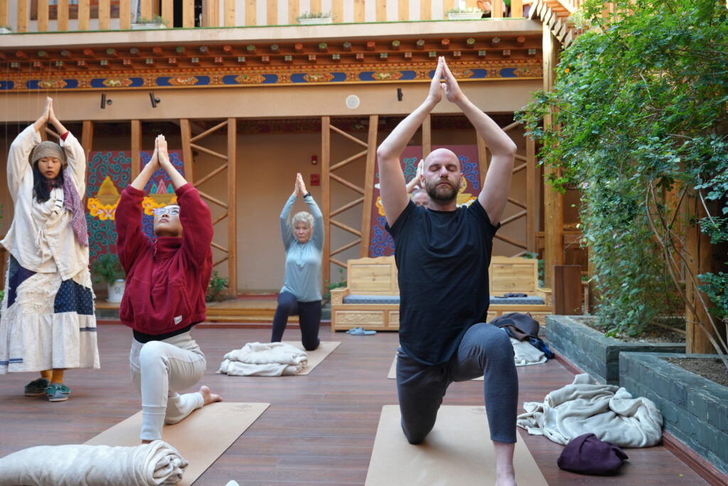 A group of people practicing yoga outdoors at a cultural site in China, with traditional wooden arch.