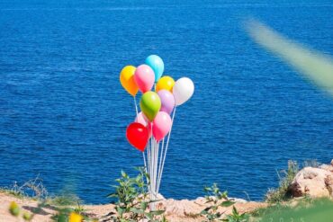 Cluster of colorful balloons tied to a weight on a rocky lakeshore with blue water in the background,Yangma Island,Yantai,Shandong,Chinatravel