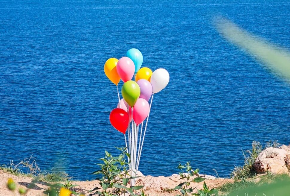 Cluster of colorful balloons tied to a weight on a rocky lakeshore with blue water in the background,Yangma Island,Yantai,Shandong,Chinatravel