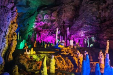 A colorful underground cave with illuminated stalactites and stalagmites in vibrant hues.