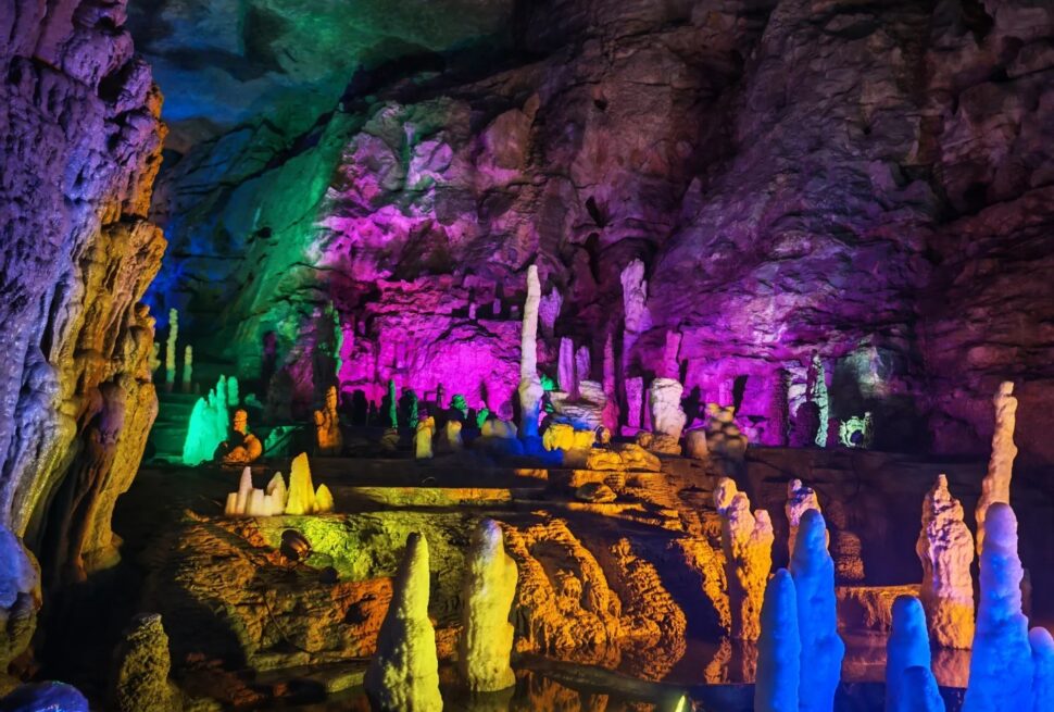 A colorful underground cave with illuminated stalactites and stalagmites in vibrant hues.