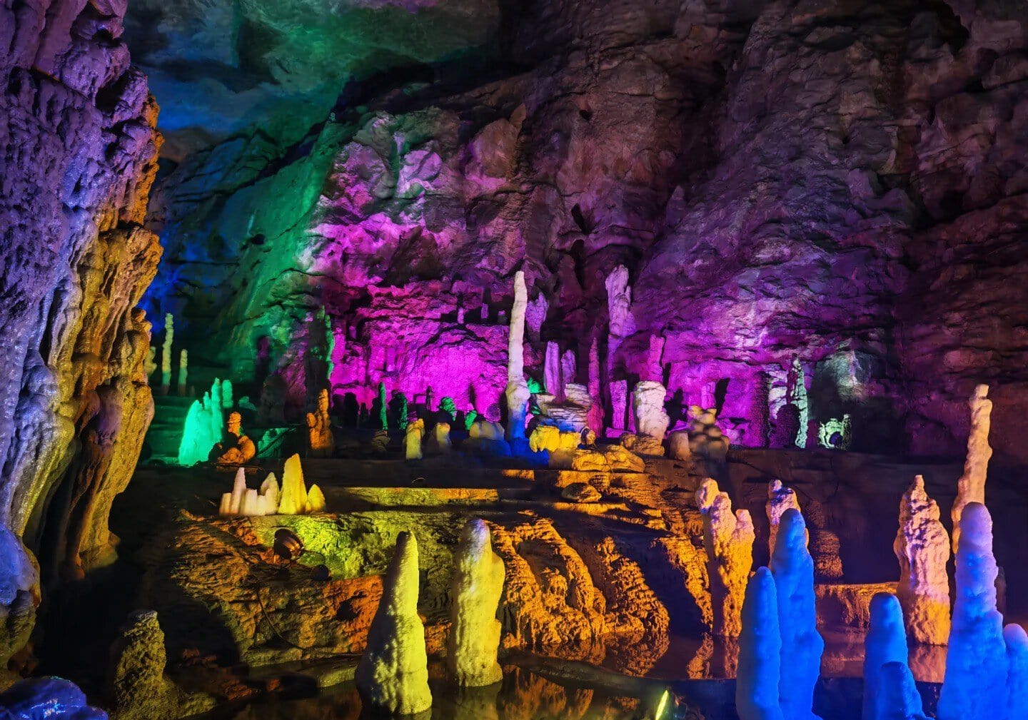 A colorful underground cave with illuminated stalactites and stalagmites in vibrant hues.