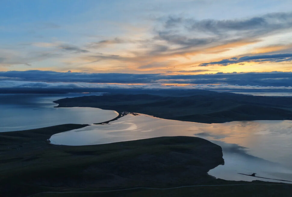 Aerial view of a winding river delta at sunset, reflecting orange and blue skies on calm water.Zaling Lake & Eling Lake,Yushu, Qinghai