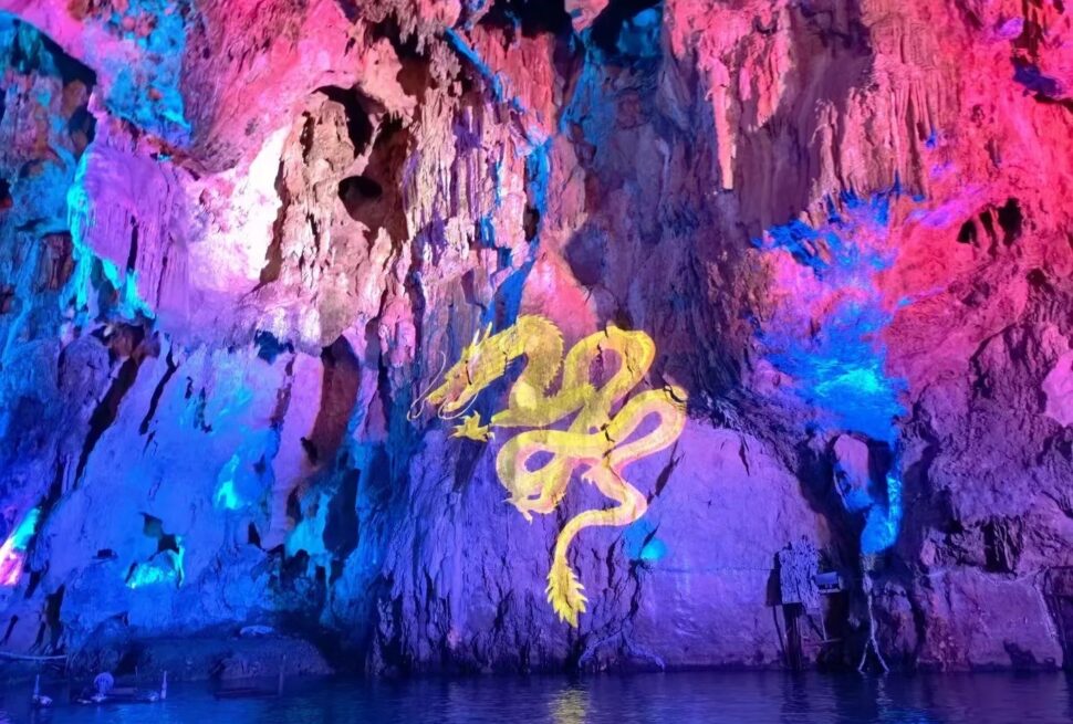 Cave wall illuminated in pink and blue with a yellow dragon mural painted on the rock, reflected in the water below.Dragon Palace Scenic Area ,Anshun,Guizhou