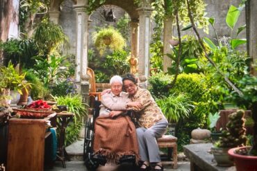 Chaoshan,Guangdong,Chinatravel A senior couple sitting together in a lush, green garden with traditional stone architecture.