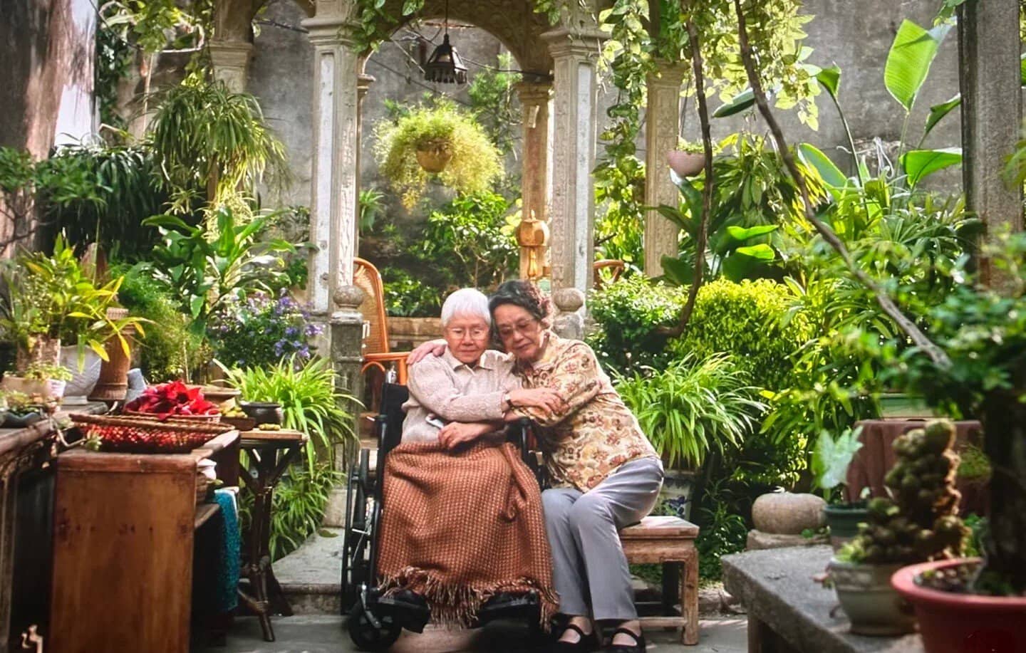 Chaoshan,Guangdong,Chinatravel A senior couple sitting together in a lush, green garden with traditional stone architecture.