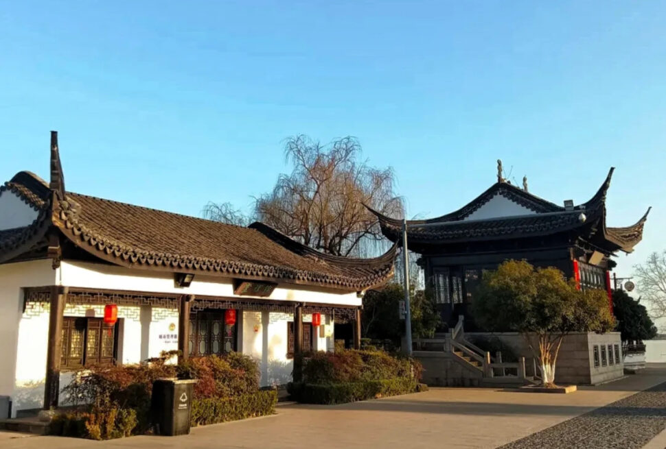 Traditional Chinese architectural complex with curved tiled roofs and red lanterns in a sunny courtyard.