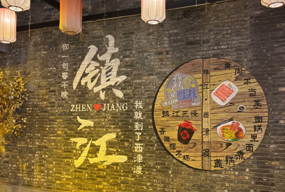 Brick wall mural with large white Chinese characters and the 'ZHEN JIANG' logo, plus a circular wooden menu showing dishes; warm lanterns hang overhead.