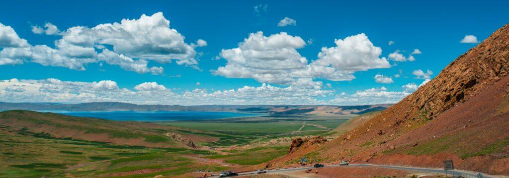 A scenic landscape of rolling green hills, a winding road, and a bright blue sky with clouds.
