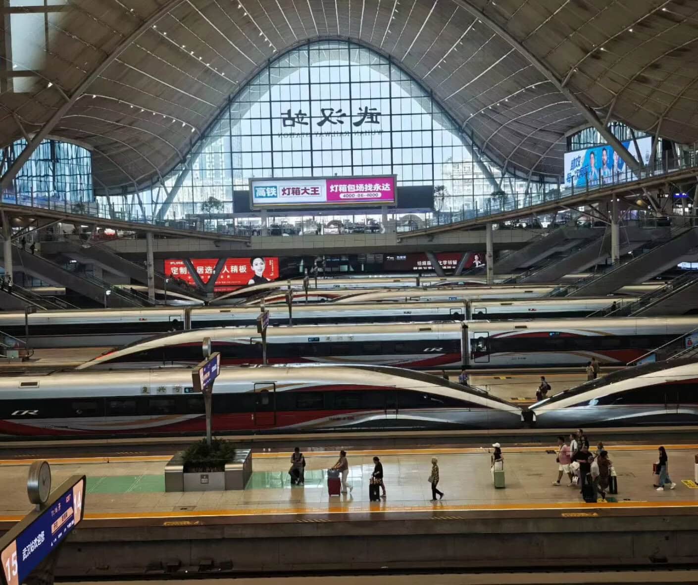 High-speed trains at a modern train station in China with a large glass roof and digital signage.