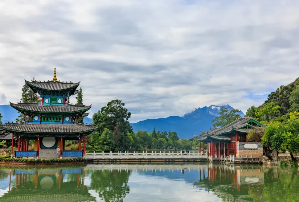 Traditional Chinese pavilion by a lake with mountains in the background.