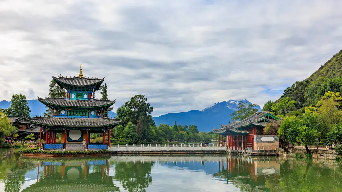 Traditional Chinese pavilion by a lake with mountains in the background.