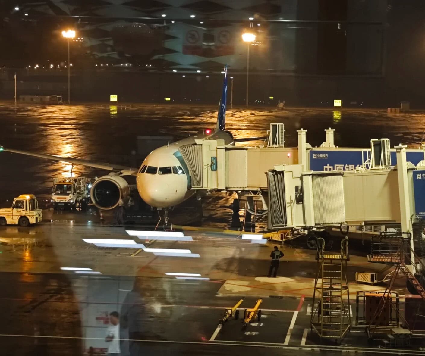Airplane at airport gate during night with wet tarmac and airport equipment.