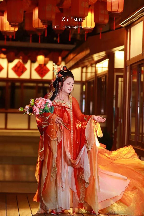 hanfu photoshoot, xingqing palace, xi'an, tang dynasty, solo, female, chinatravel, Woman in an ornate orange traditional Chinese dress holding a pink bouquet, standing under red lanterns during a performance.